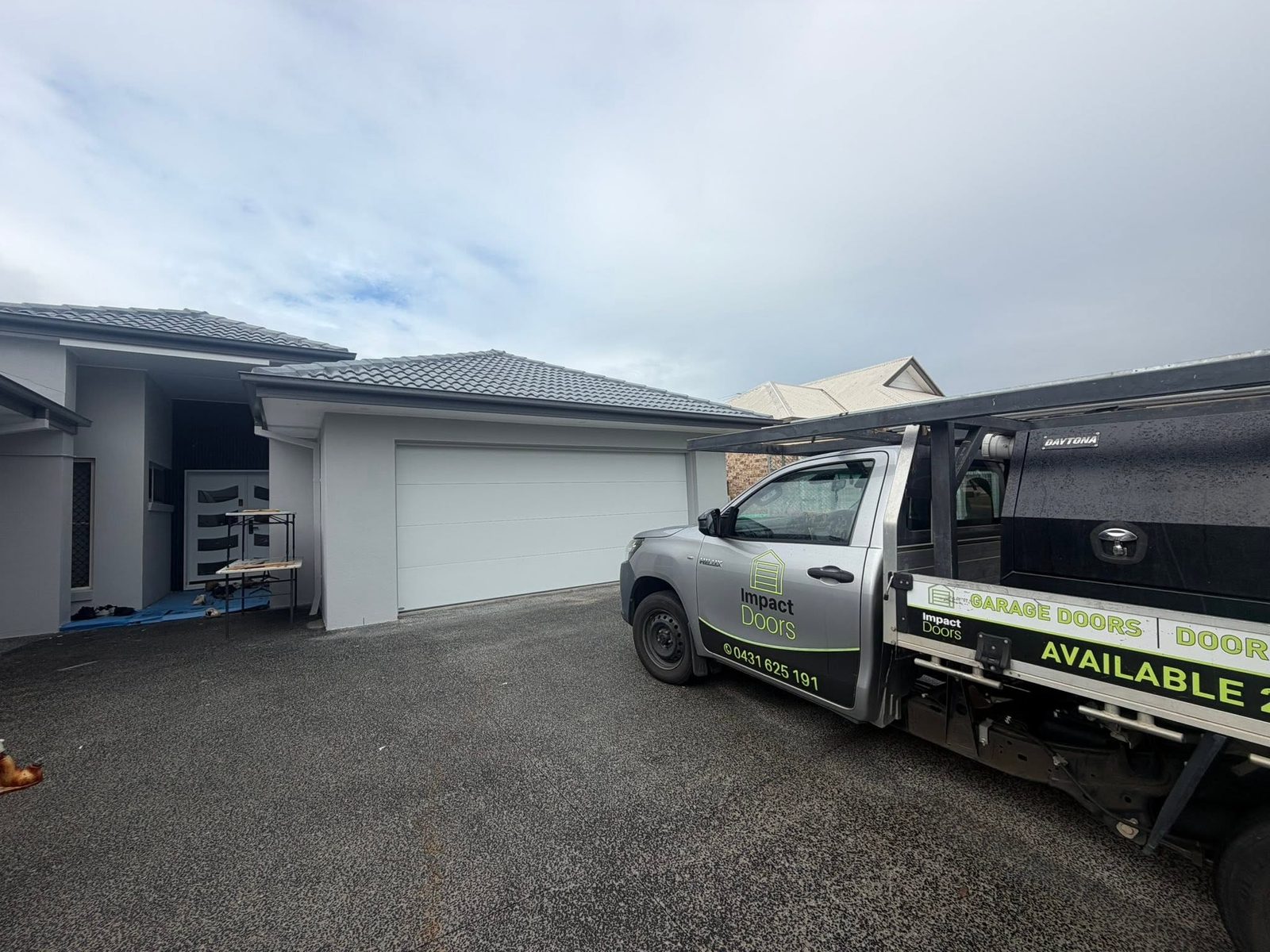 The branded Impact Doors ute with its signwritten tray visible, parked in front of a new white sectional garage door.