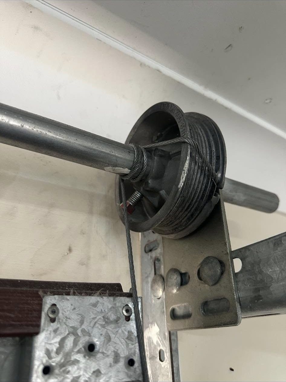 Close-up of a garage door cable drum and torsion spring shaft with the lift cable wound onto the drum.