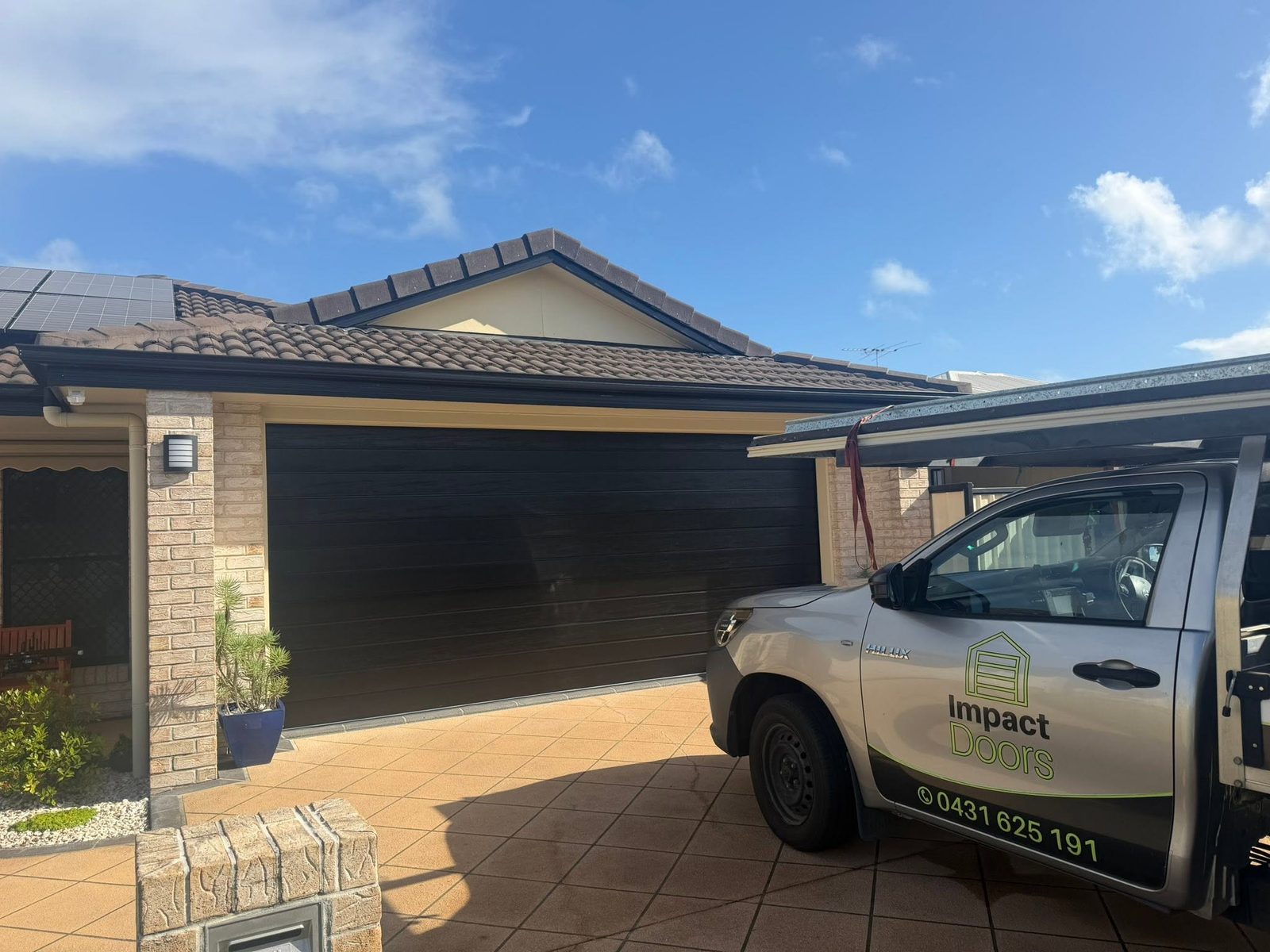 The branded Impact Doors ute parked in the driveway in front of a dark sectional garage door on a brick home.