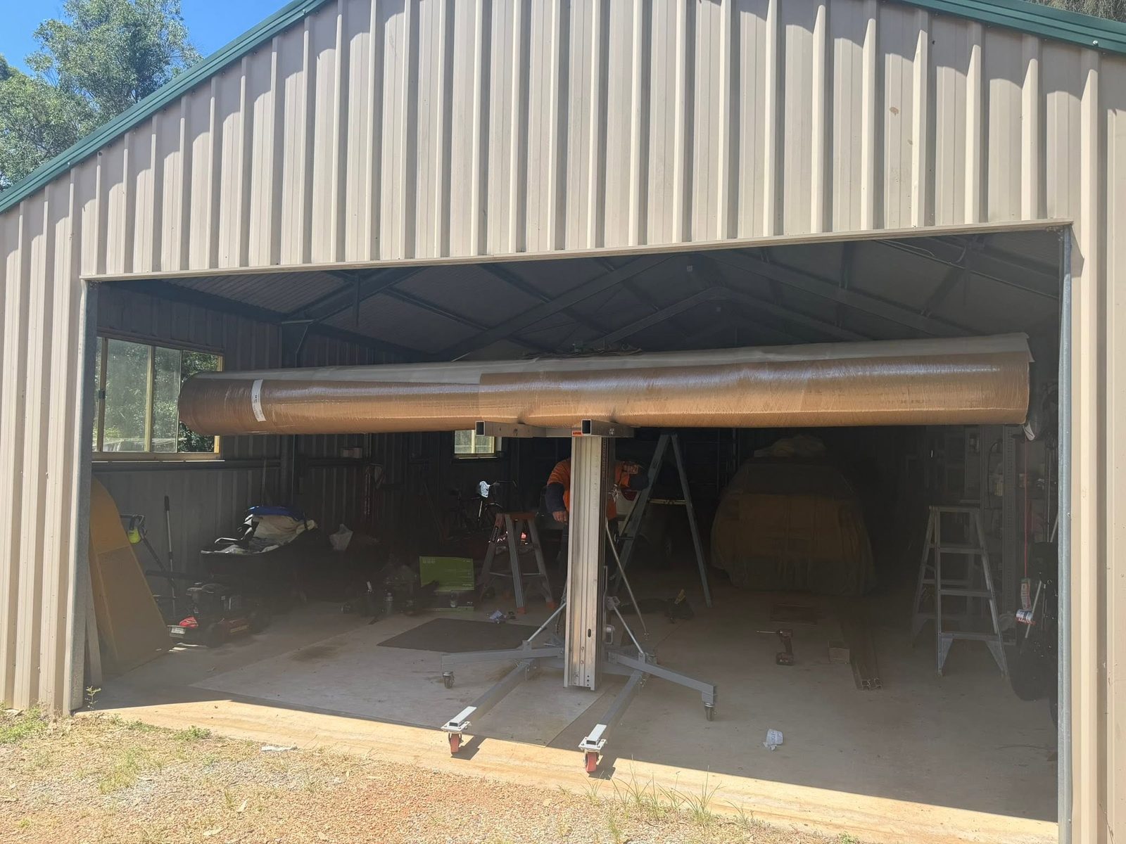 A new roller door being installed on a Colorbond shed, with the wrapped door curtain lifted into position on a door jack.