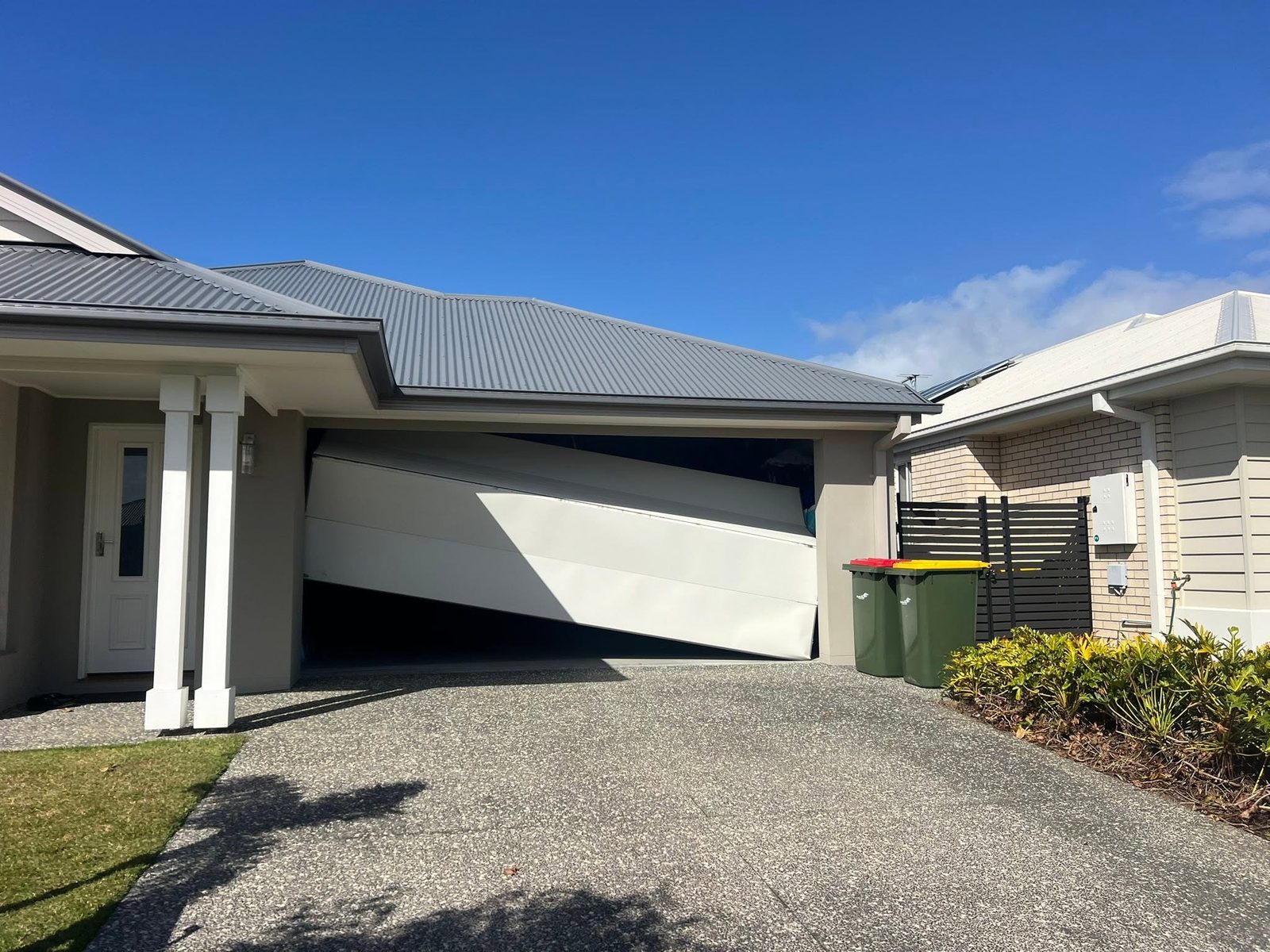 A sectional garage door hanging off its track and sitting on an angle, seen from the driveway of a Queensland home.